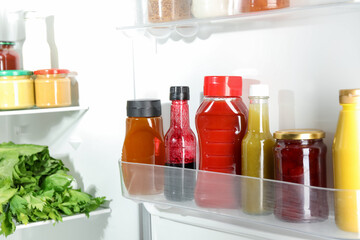 Bottles with different tasty sauces and products in fridge, closeup