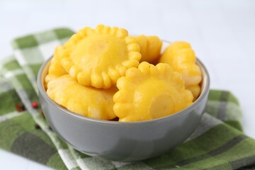 Pickled pattypan squashes in bowl and towel on white table, closeup