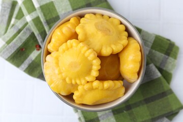 Pickled pattypan squashes in bowl and towel on white tiled table, top view