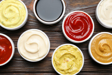 Different sauces in bowls on wooden table, flat lay