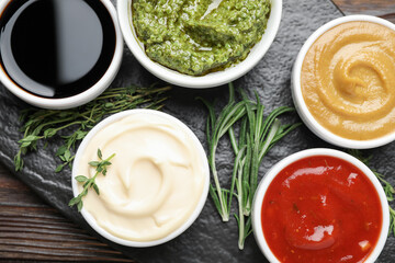 Different sauces and herbs on wooden table, flat lay