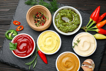 Different sauces and herbs on wooden table, flat lay