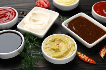 Different sauces and herbs on wooden table, closeup