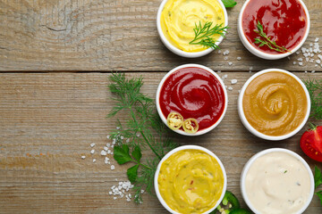 Different sauces and herbs on wooden table, flat lay. Space for text