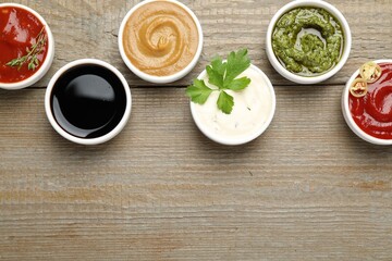 Different sauces and parsley on wooden table, flat lay. Space for text