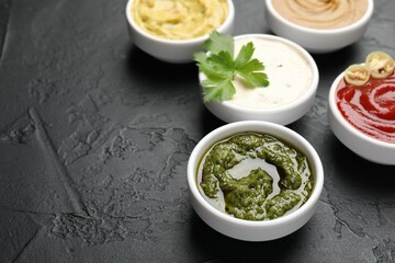 Different sauces and parsley on black table, closeup. Space for text