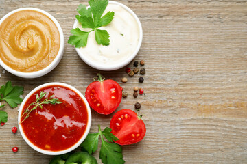 Different sauces, spices and parsley on wooden table, flat lay. Space for text