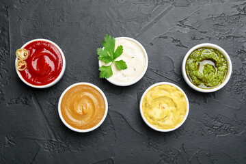 Different sauces and parsley on black table, flat lay