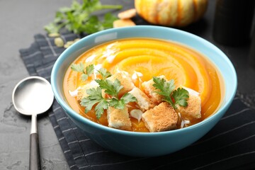 Tasty pumpkin cream soup with parsley and croutons served on dark textured table, closeup