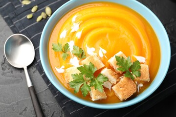 Tasty pumpkin cream soup with parsley and croutons served on dark textured table, closeup