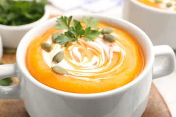 Tasty pumpkin cream soup with parsley and seeds in bowl on table, closeup