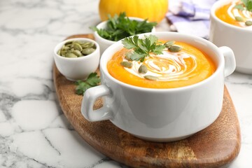 Tasty pumpkin cream soup with parsley and seeds in bowl on white marble table, closeup