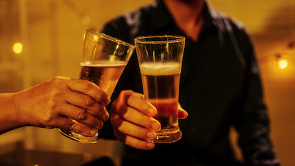Close up friends hands clinking beer glasses in warm golden light, celebrating friendship teamwork. A joyful moment filled with laughter, unity, positive energy during relaxing evening gathering.