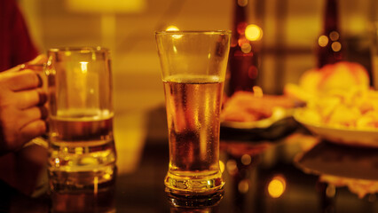 Close up friends hands clinking beer glasses in warm golden light, celebrating friendship teamwork. A joyful moment filled with laughter, unity, positive energy during relaxing evening gathering.