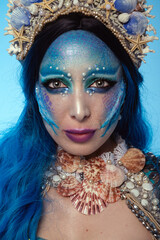 Portrait of an attractive woman with mermaid makeup, blue hair, and a seashell crown.