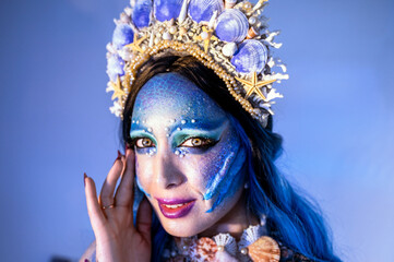 Portrait of an attractive woman with mermaid makeup, blue hair, and a seashell crown.