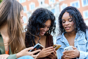 Three young women sharing content on their smartphones outdoors