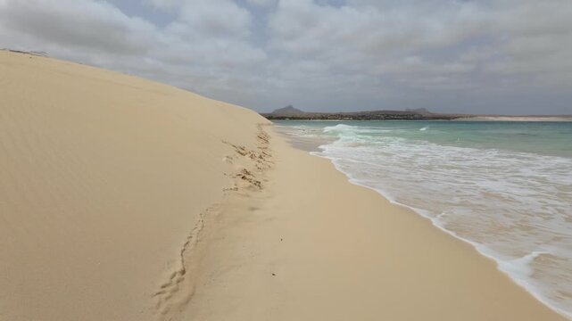 Waves breaking against sand dunes as they meet the sea on the shoreline of the Cape Verde island of Boa Vista.