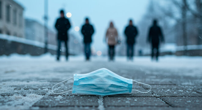 Medical mask on snow-covered street with blurred pedestrians walking  