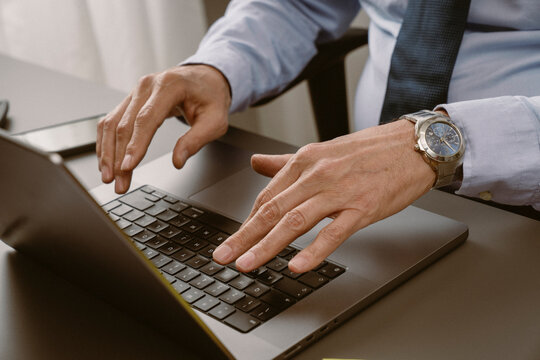 Professional man typing on laptop at office desk with smartphone and notepad during work hours