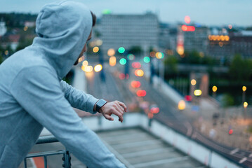 Athlete in hoodie resting outdoors overlooking city at twilight