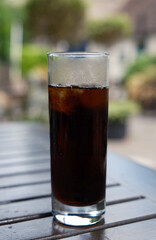 Cold glass of cola with ice cubes on a wooden outdoor table on a sunny day.