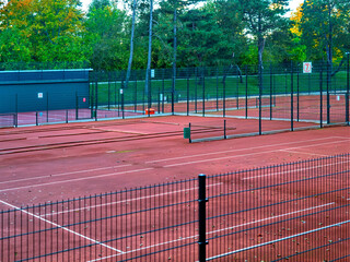 Outdoor padel tennis courts in a sports club, fenced with metal nets, on a cloudy autumn day. The red clay courts are empty,