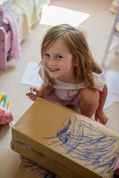 Smiling child drawing creatively on a cardboard box indoors