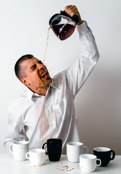Stressed man in office pouring coffee over himself in frustration
