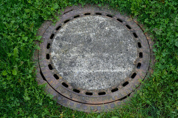 Old manhole cover surrounded by green grass
