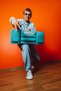 Man in blue outfit holding boombox in front of orange wall having fun