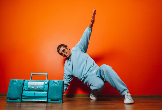 Breakdancer in blue tracksuit with boombox posing by orange wall