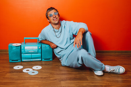 Man in blue tracksuit relaxing with boombox and CDs against orange wall