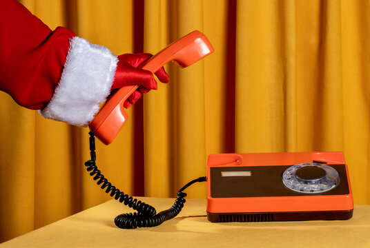 Santa gloved hand holding retro orange phone in festive indoor setting