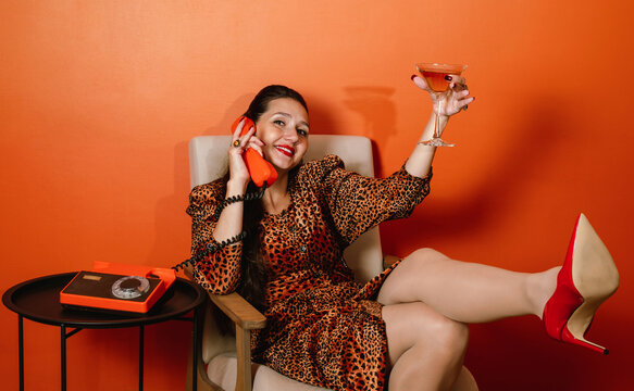 Portrait of woman in leopard print dress celebrating with cocktail and phone