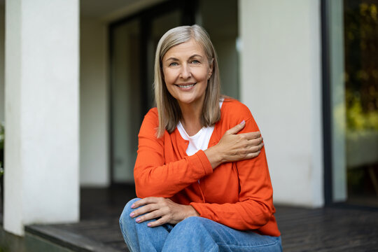 Senior good-looking woman sitting on the steps of her house and feeling contented