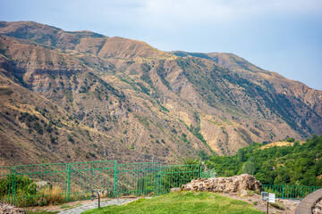 Fototapeta premium Panoramic view of the rugged Garni Gorge mountains in Armenia, showcasing the dry golden slopes and sparse green vegetation under a bright summer sky