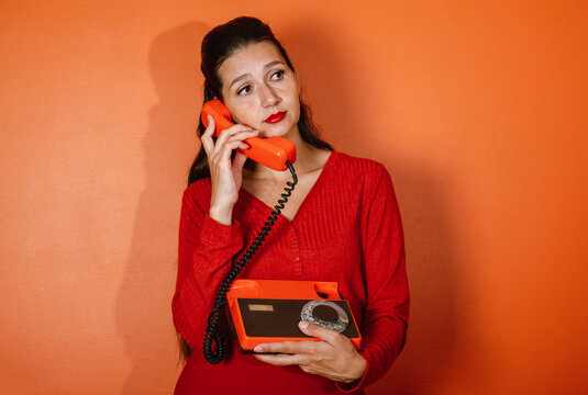Portrait of thoughtful woman holding retro orange rotary phone indoors