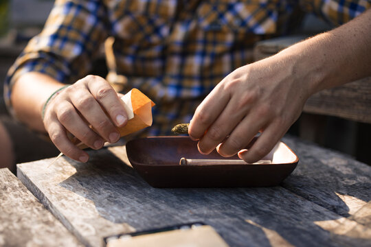 Man preparing cigarette with dried marijuana leaves at table