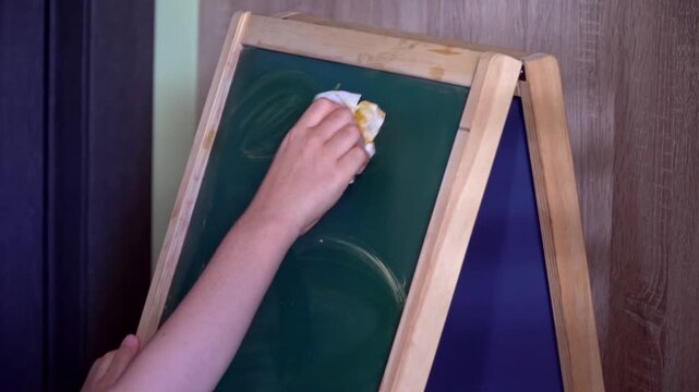 Top view closeup of a 9-year-old child cleaning chalkboard with rag at home.