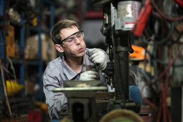 White man technician checking used car damaged engine block at scrap yard warehouse recycle area part. Maintenance engineer inspecting rust oily auto motor old spare part in junkyard for reuse service
