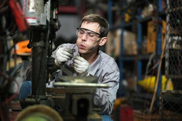 White man technician checking used car damaged engine block at scrap yard warehouse recycle area part. Maintenance engineer inspecting rust oily auto motor old spare part in junkyard for reuse service