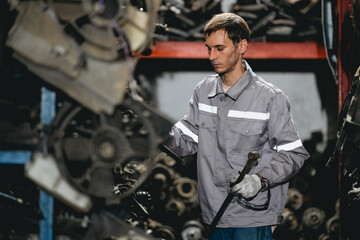 White man technician checking used car damaged engine block at scrap yard warehouse recycle area part. Maintenance engineer inspecting rust oily auto motor old spare part in junkyard for reuse service