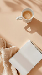Minimalist workspace featuring a blank notepad, a cup of coffee, and soft fabric draped on a warm-toned surface, creating a serene and inviting atmosphere for creativity