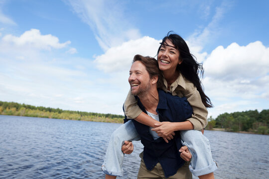 Couple enjoying piggyback ride by the water on a windy day