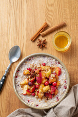 Overnight oatmeal with apple, cranberry and cinnamon in a plate on a wooden background with honey