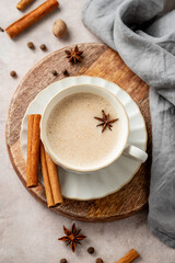 Traditional Indian masala chai tea with milk and spices in a white cup on a wooden board on a light background