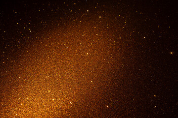 Shimmering golden glitter texture glowing diagonally, sparkling particles shine vividly and dissolve into dark edges forming luxurious abstract backdrop