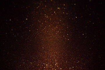 Deep brown glitter texture bathed in shadow, faint beam of light in the center softly reveals golden sparkles shimmering