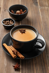Traditional Indian masala chai tea with milk and spices in a black cup on a dark wooden background
